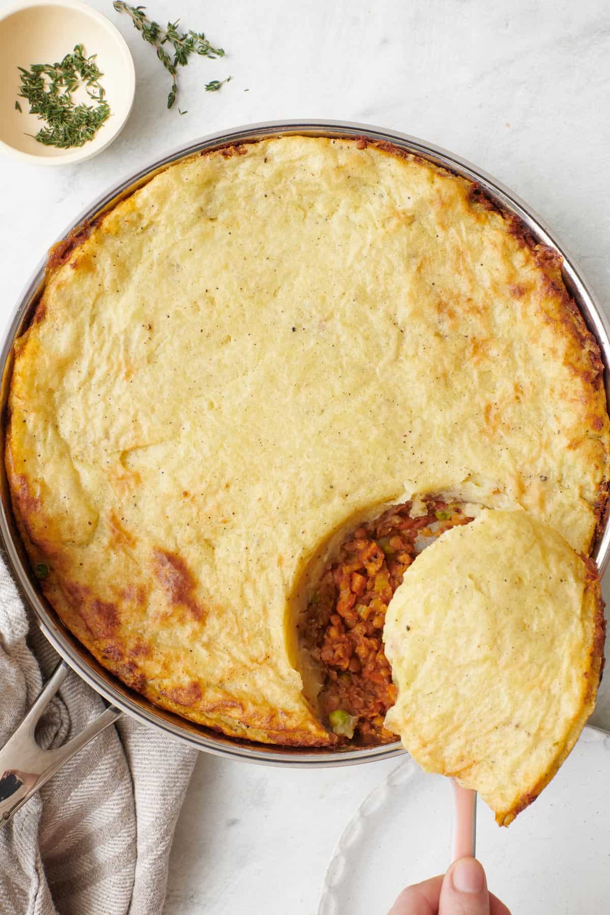Baked Lentil Shepherd's pie in a skillet with a serving being scooped out.