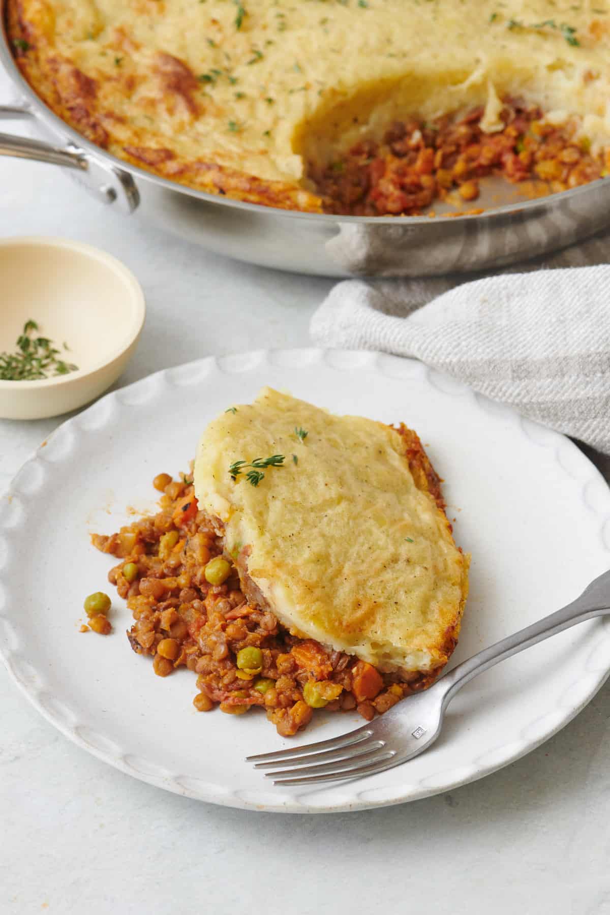 Serving of lentil shepherd's pie on a small plate with a fork and the skillet of recipe nearby.