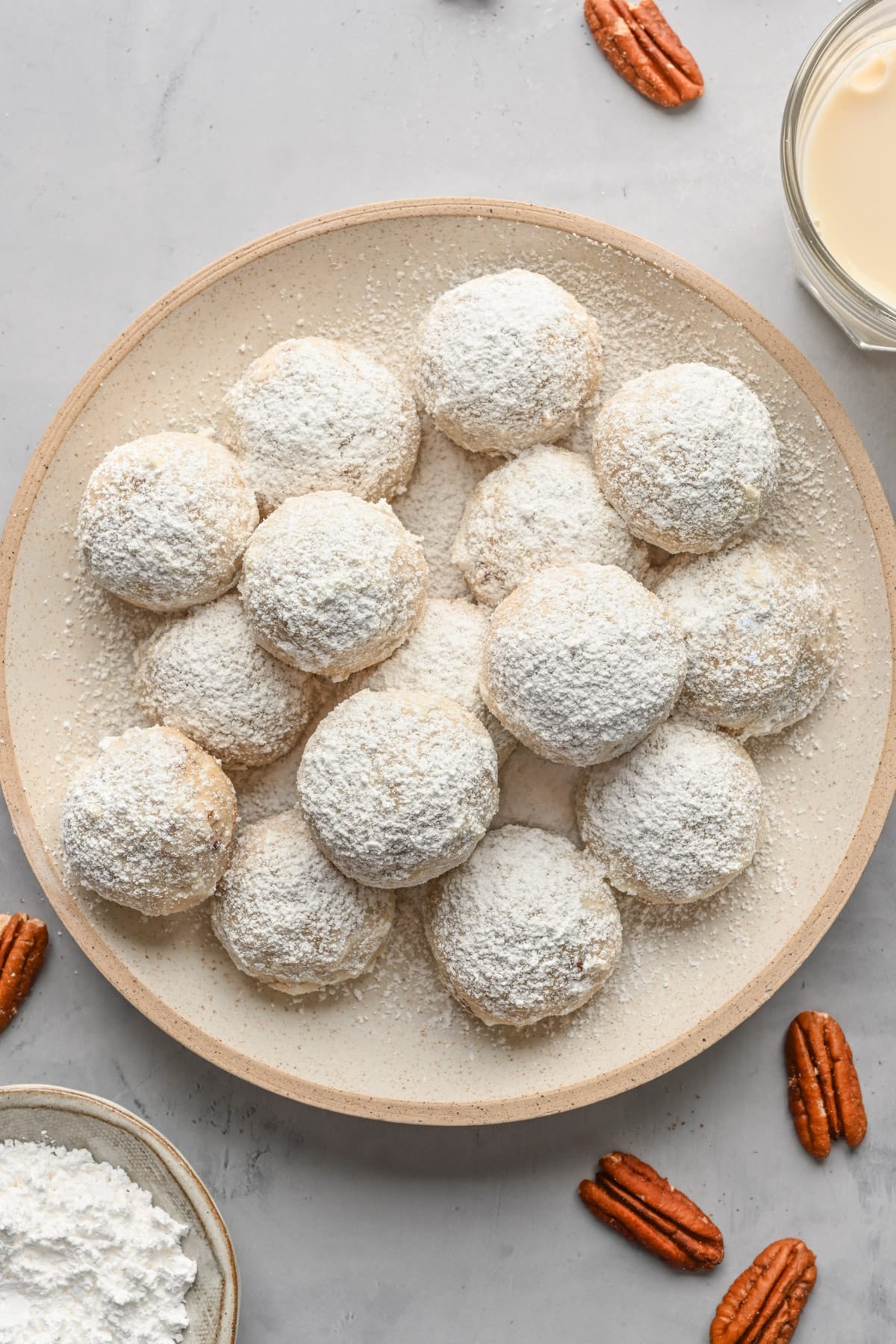 Pecan snowball cookies on a plate with more pecans around.