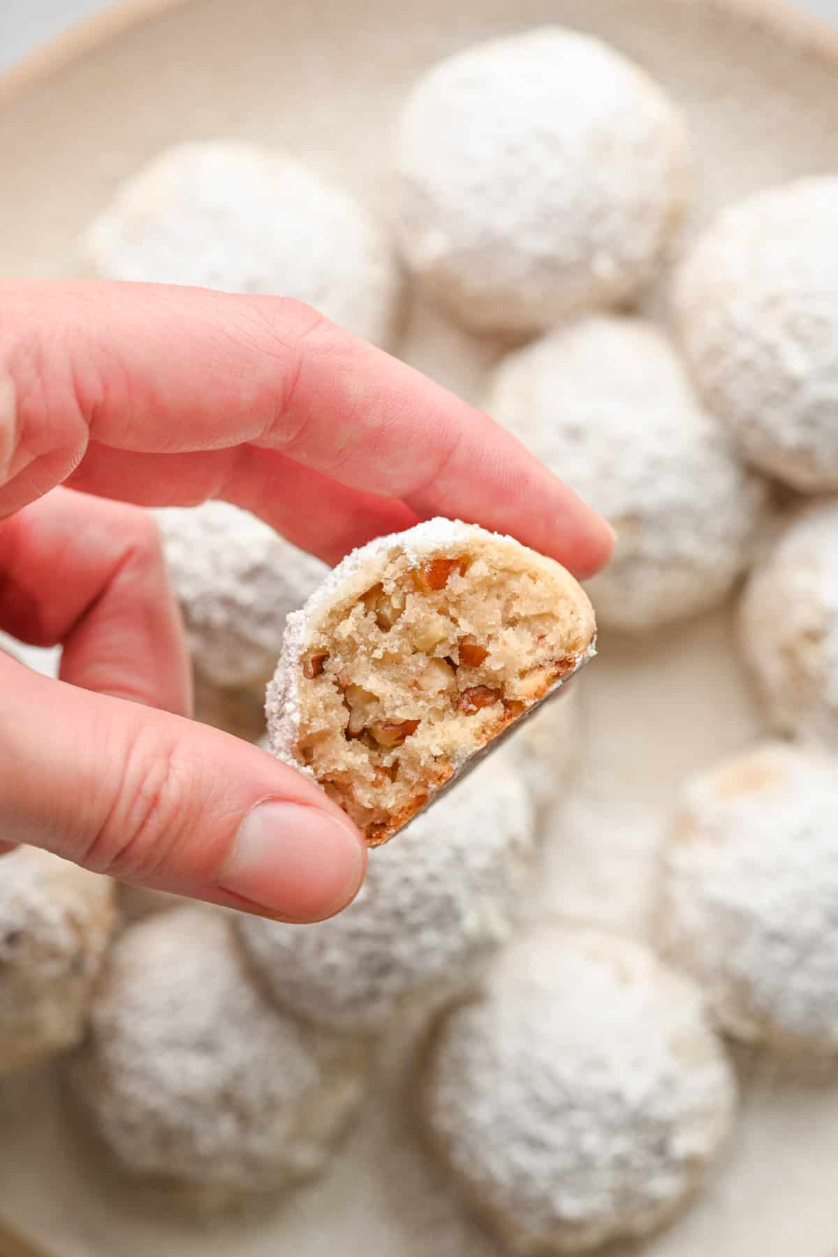 Hand holding a pecan snowball cookie with a bite taken out to show inside texture.