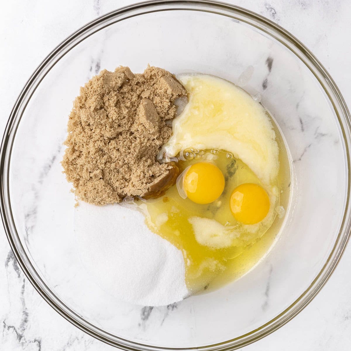 Sugars, oil, butter, and eggs in a bowl before whisking.