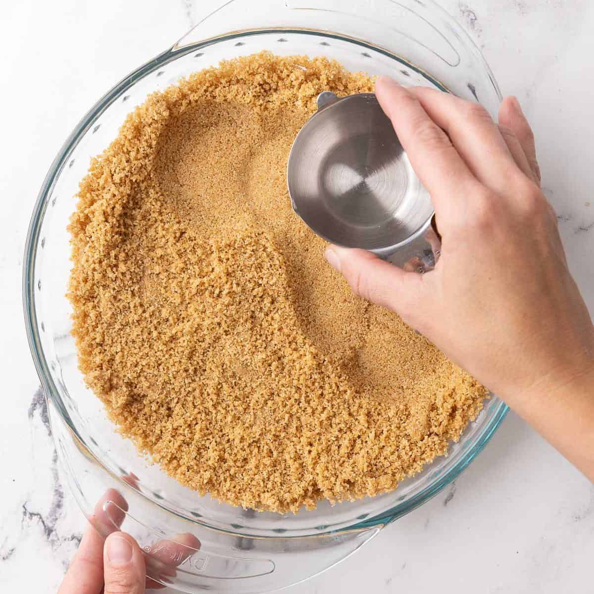 Crumbs added to a pie plate and just starting to be pressed into an even layer.