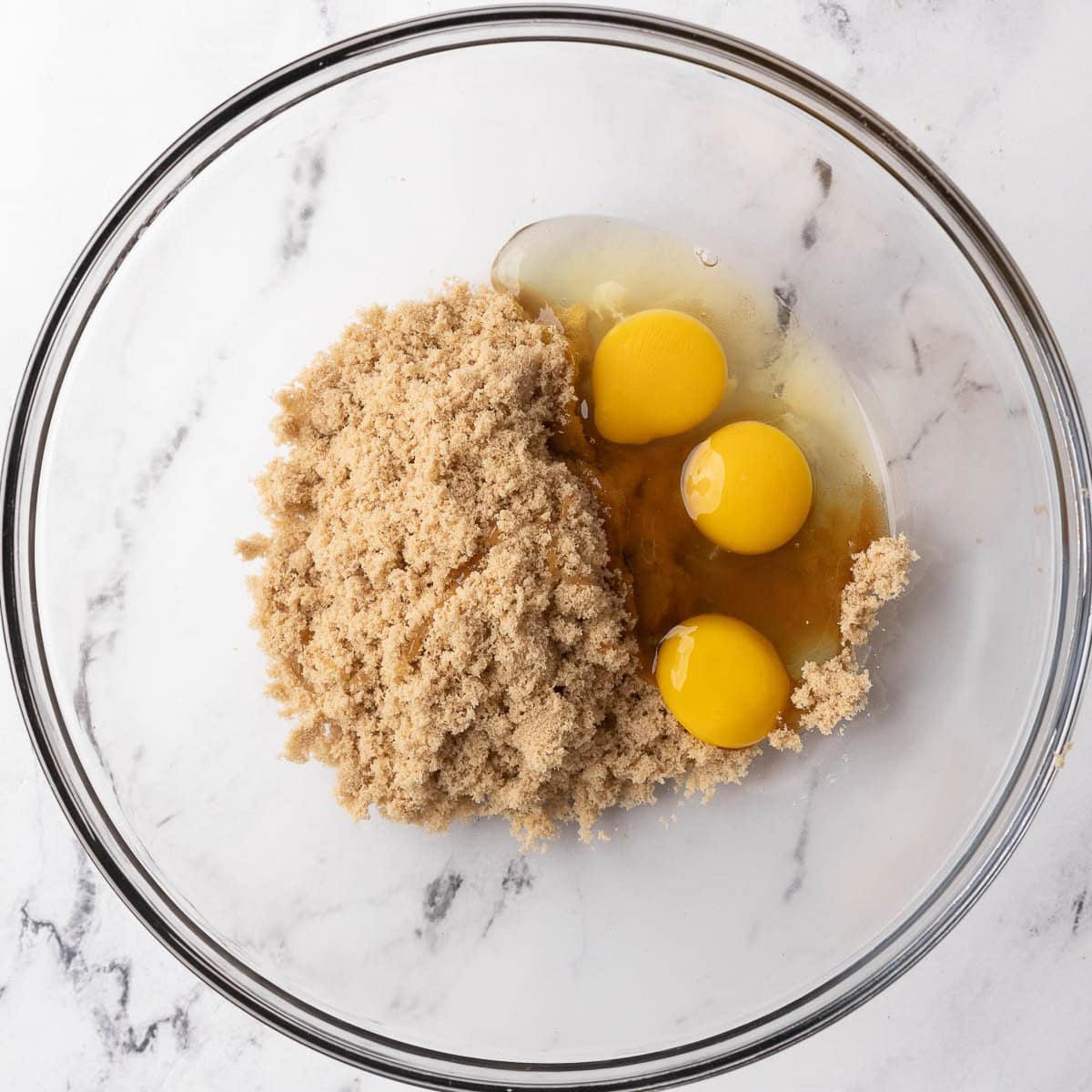 Eggs, egg yolk, and brown sugar in a bowl before mixing.