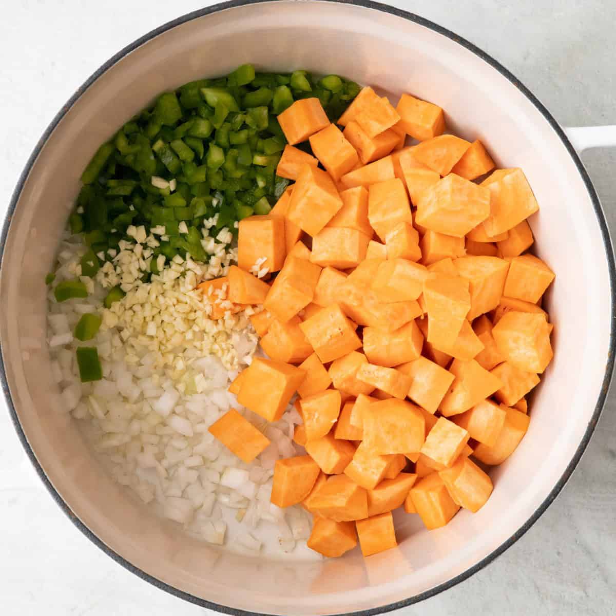 Onions, sweet potatoes, bell pepper, garlic in a pot after cooking.