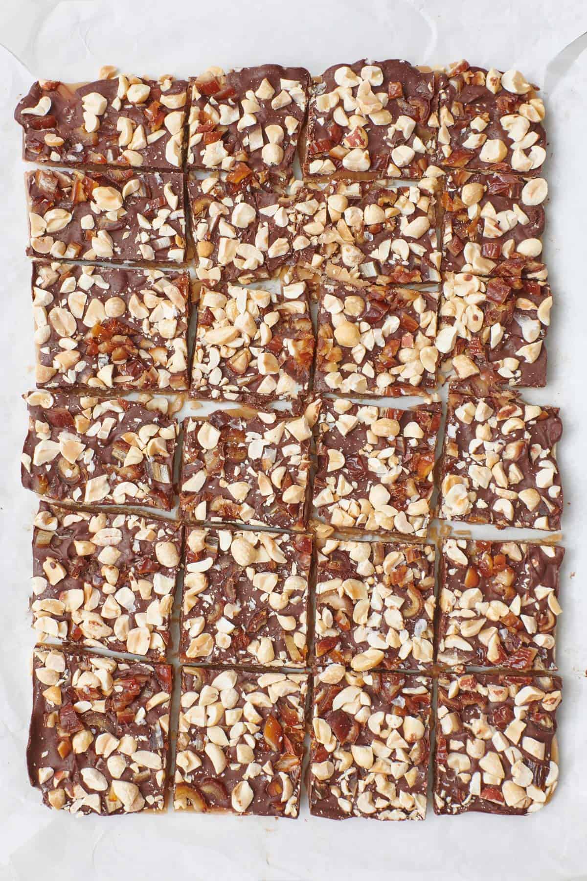 Peanut and chopped date covered homemade toffee cut into squares on parchment paper.