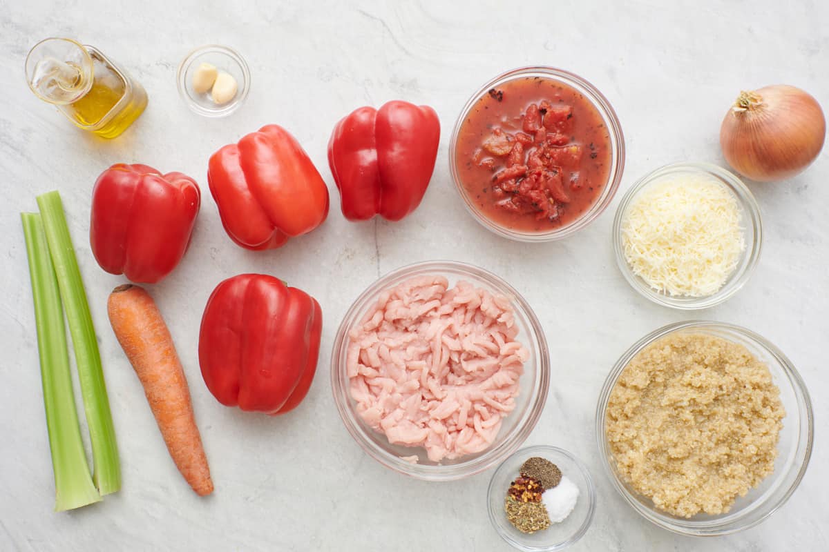Ingredients for recipe before prepping: celery, red bell peppers, carrot, garlic oil, raw ground turkey in a glass bowl, fire roasted diced tomatoes, mozzarella cheese, cooked quinoa, spices, and onion.