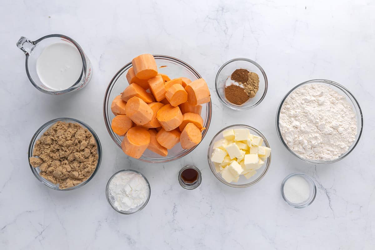 Ingredients for recipe in individual bowls: coconut milk, brown sugar, sweet potato chunks, cornstarch, vanilla, vegan butter, spices, flour, and salt.