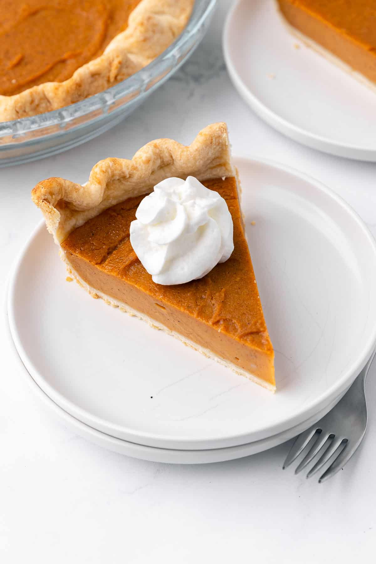 Slice of vegan sweet potato pie on a plate with a dollop of whipped cream on top.