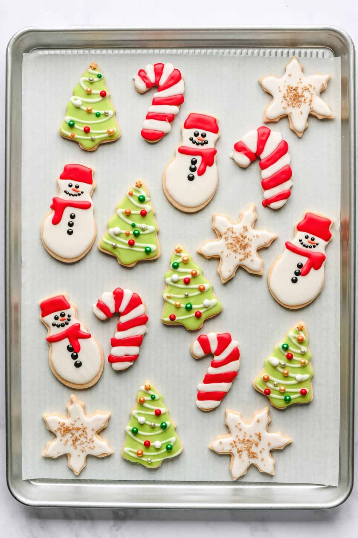 Cut out Christmas cookies on a parchment lined baking sheet decorated with holiday colors.