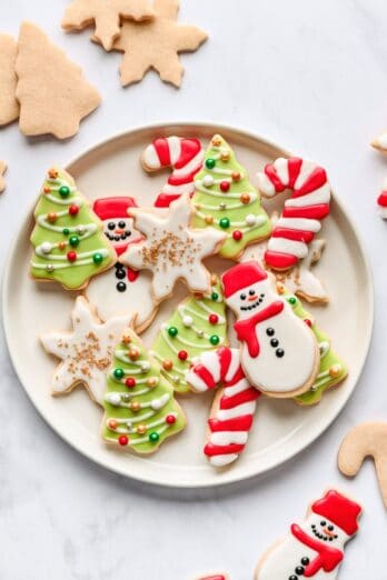 Christmas sugar cookies on a round plate with undecorated cut out cookies around.