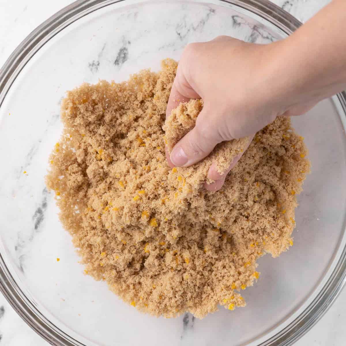 Brown sugar with orange zest in a bowl with hand massaging together.