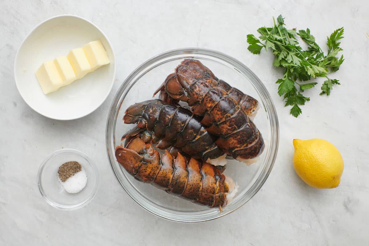 Ingredients for recipe before prepping: butter, salt and pepper, lobster tails, fresh parsley, and lemon.