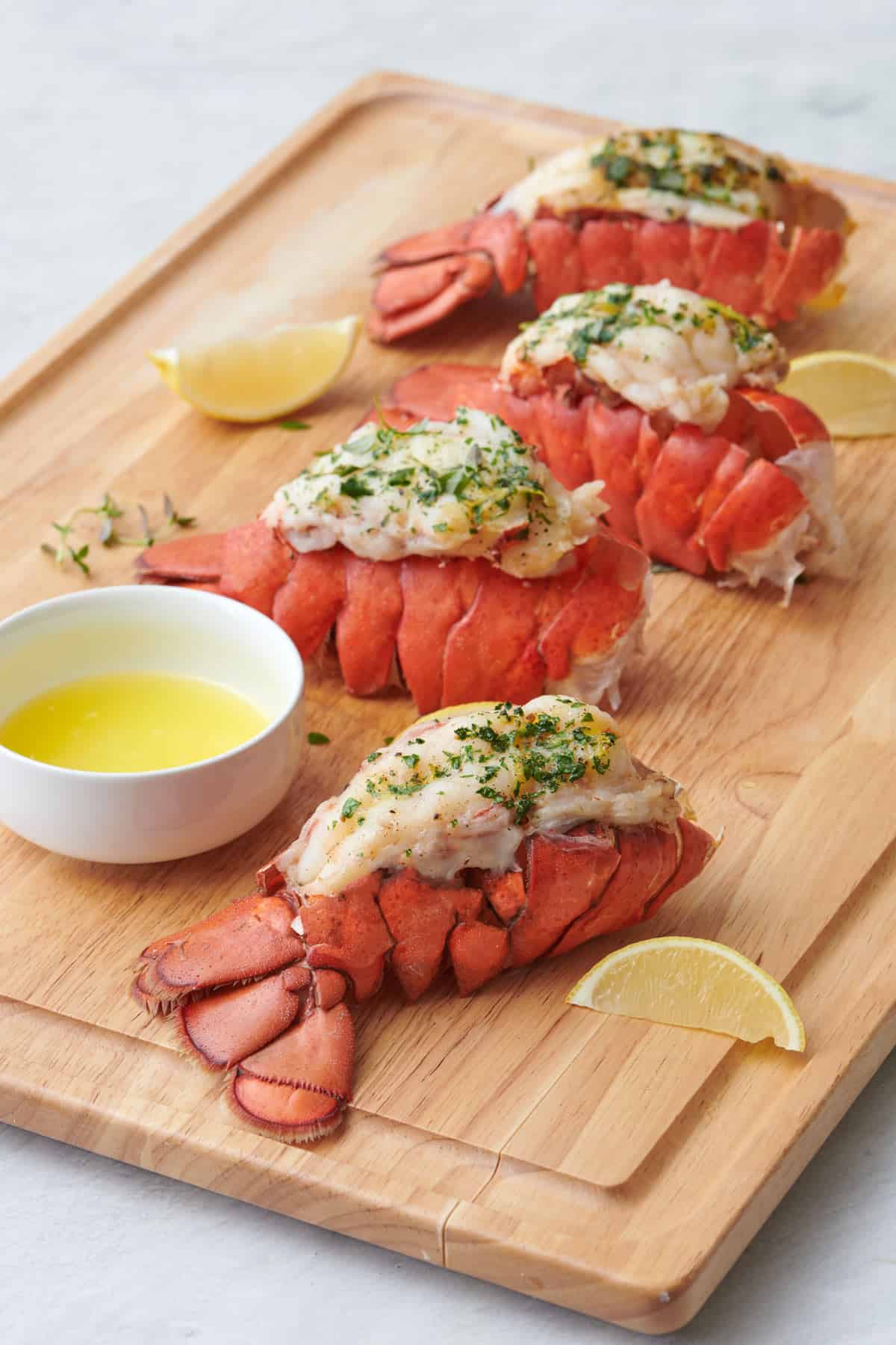 Lobster tails on a cutting board cooked 4 different ways: baked, air fried, steamed, and grilled.