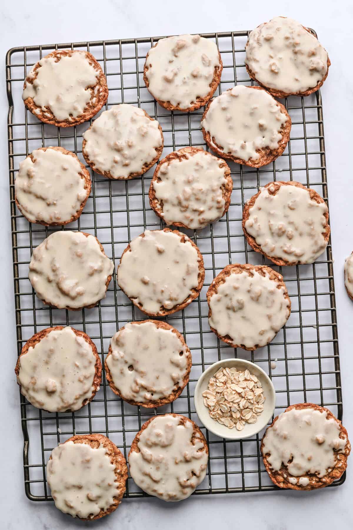 Iced oatmeal cookies on a wire rack with a small dish of oats.