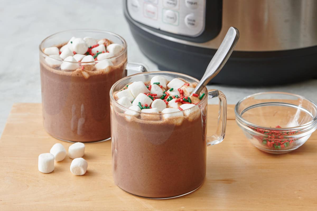 Instant pot hot chocolate served in two glass mugs and topped with mini marshmallows with holiday sprinkles on top.