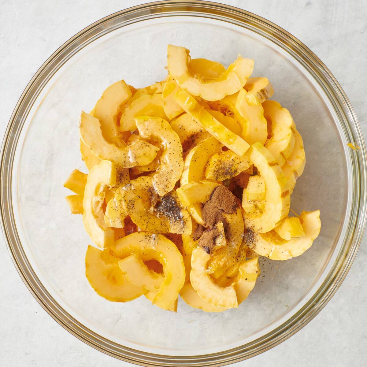 Squash slices in bowl with oil and spices added, before tossing together.