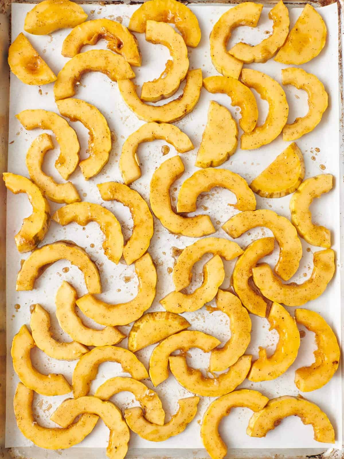 Seasoned squash slices in an even layer before baking on one of the baking sheets.