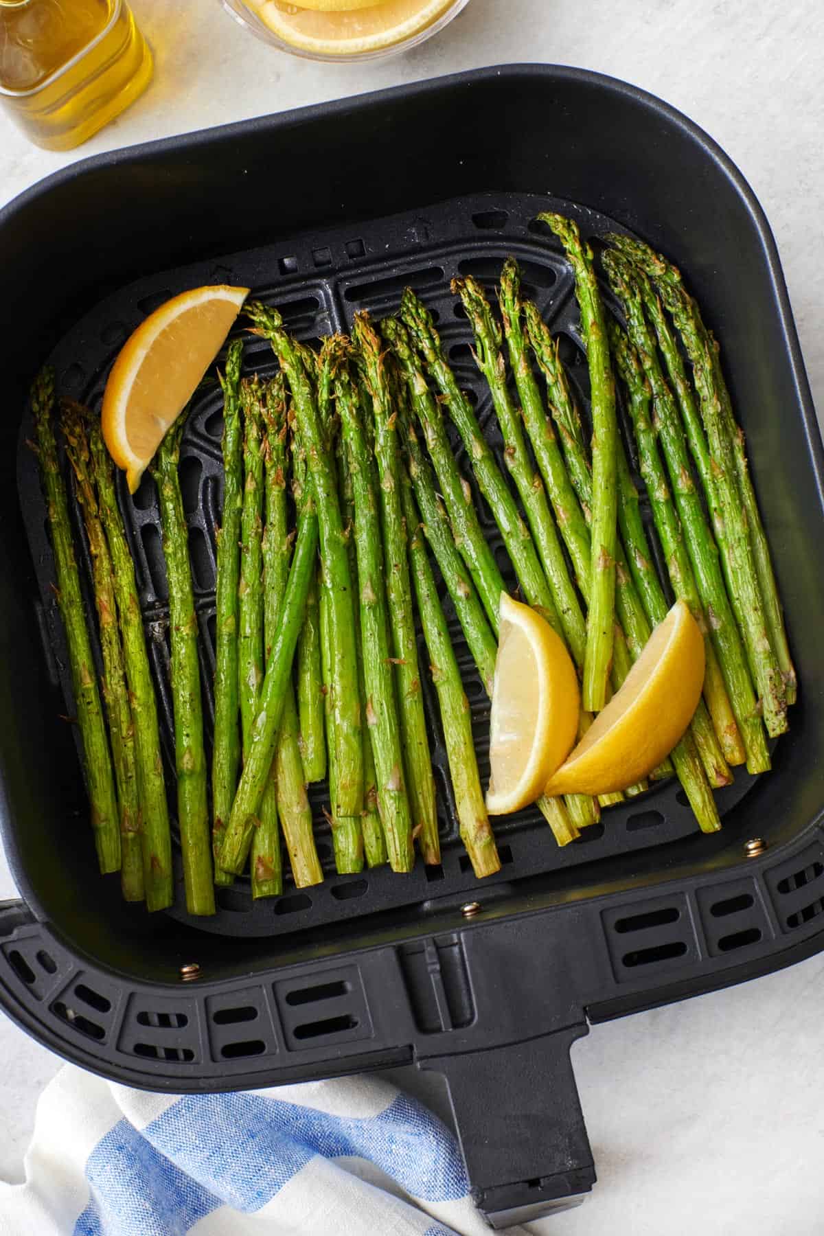 Air fryer asparagus in the air fryer basket garnished with lemon wedges.