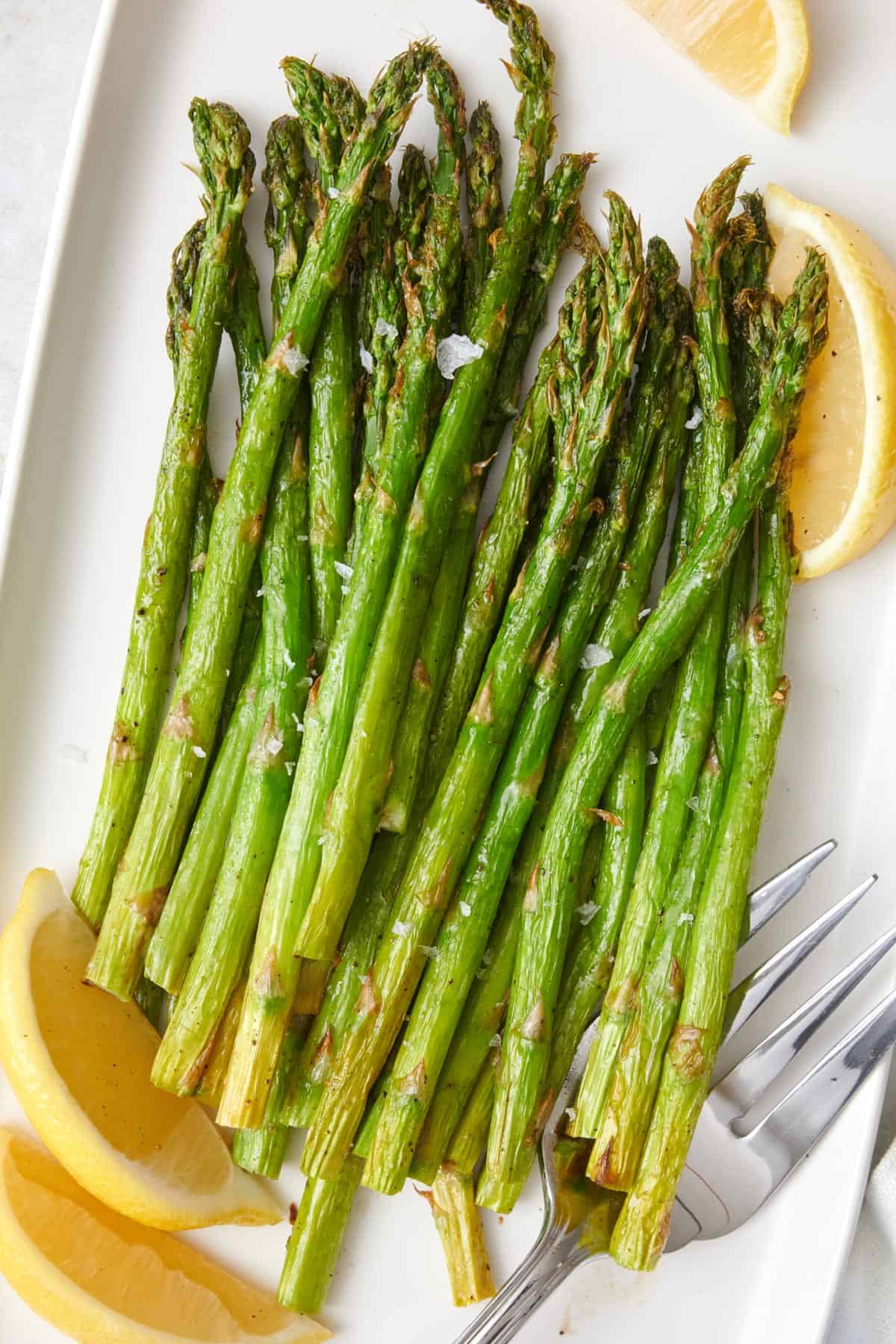 Air fried asparagus on a serving platter, garnished with fresh lemon wedges.