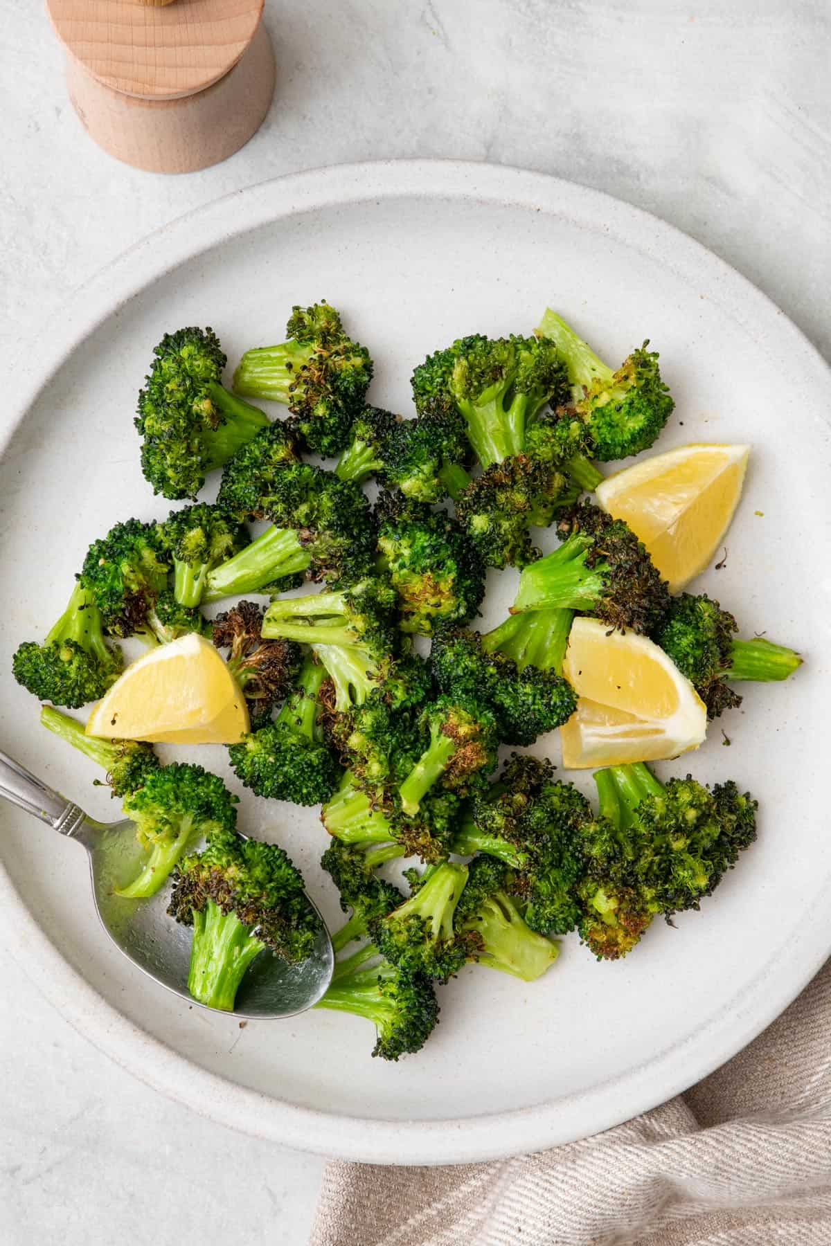 Air fryer broccoli on a plate with lemon wedges.
