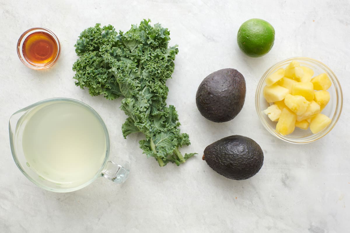 Ingredients for recipe: honey, coconut water, kale, 2 avocados, lime, and pineapple chunks.