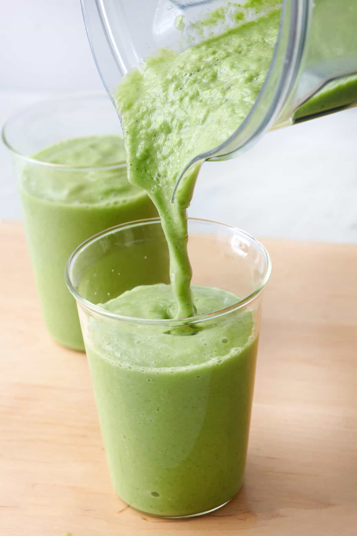 Avocado smoothie being poured into two glasses from blender.