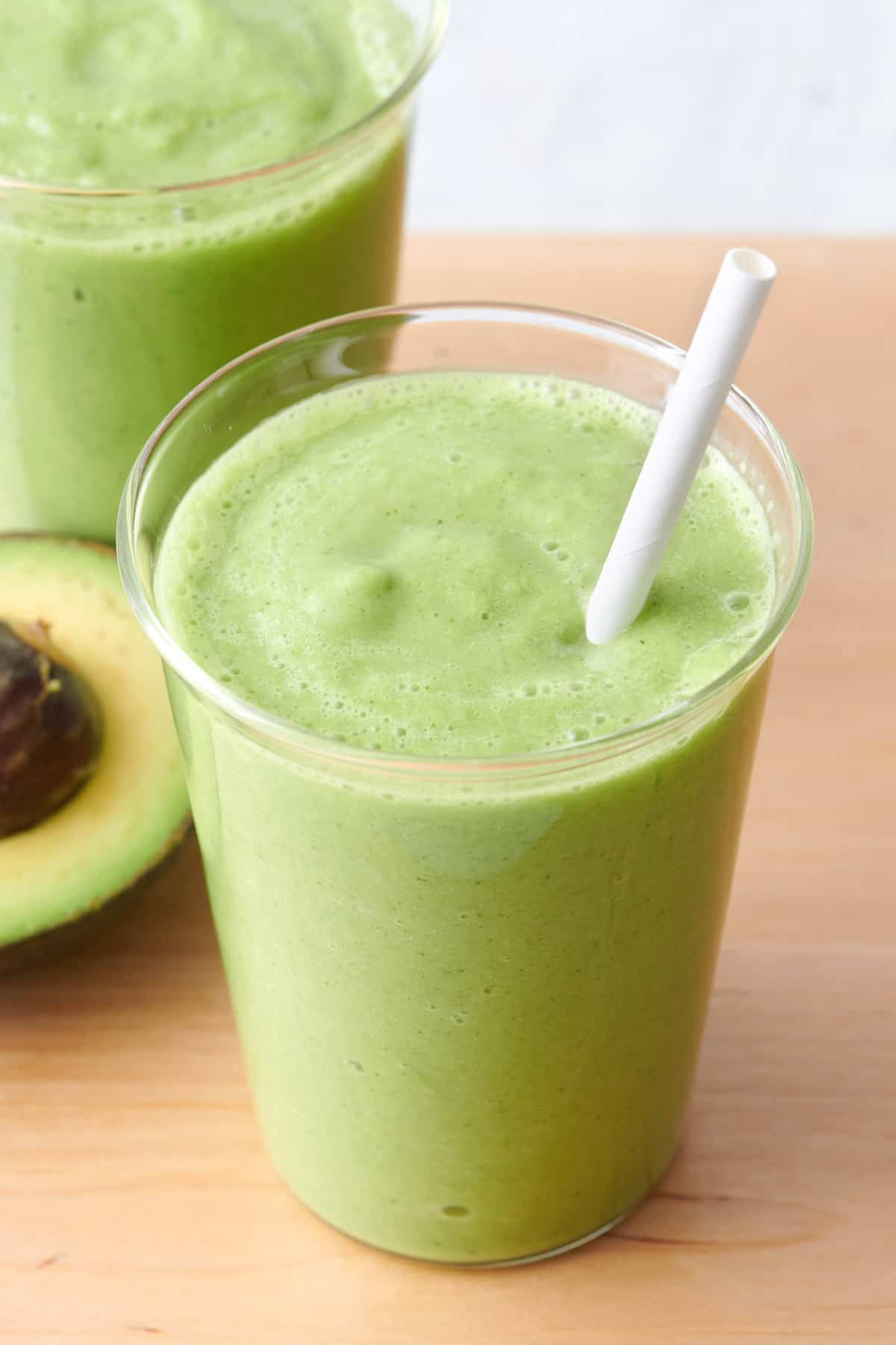 Avocado smoothie in a clear class with a straw dipped in.