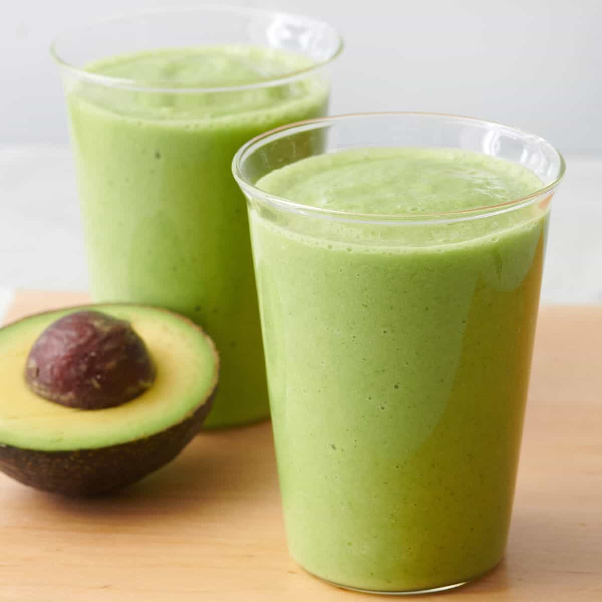 Two cups of avocado smoothie with half avocado nearby.