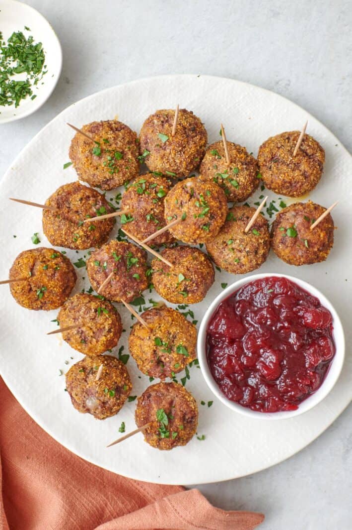Brie cheese stuffed meatballs on a serving plate with toothpicks in each one for dipping into the small dish of cranberry sauce.
