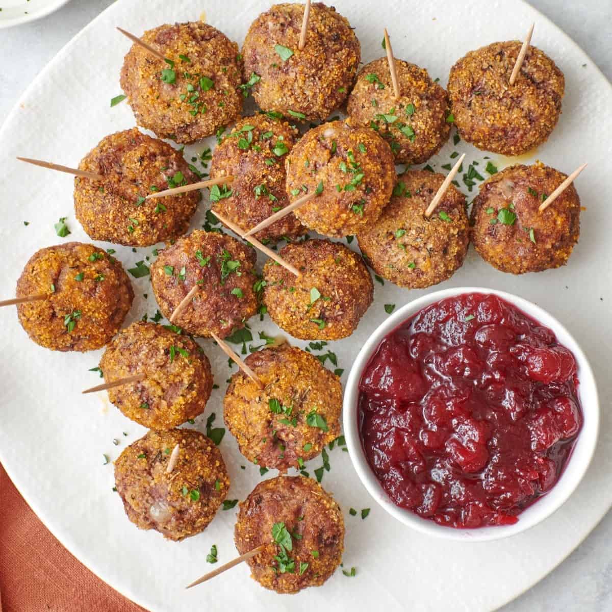 Brie cheese stuffed meatballs with toothpicks in each one and a small dish of cranberry sauce.