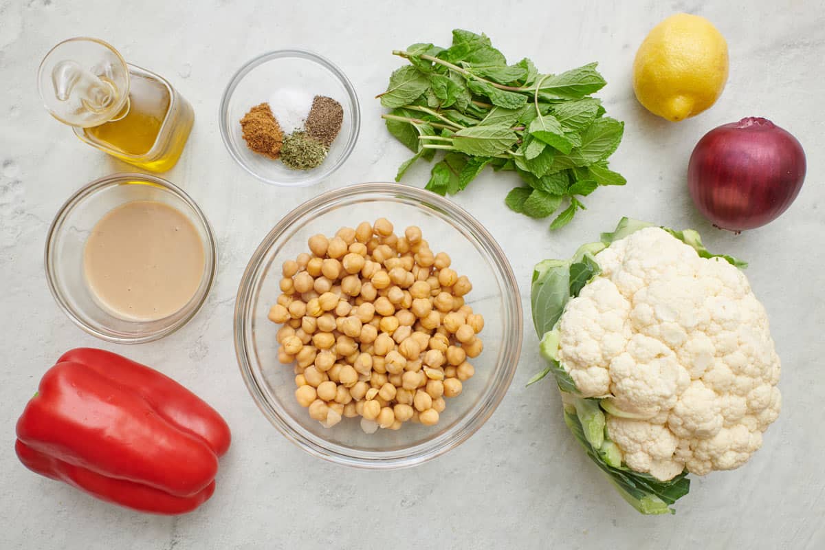 Ingredients to make cauliflower salad: cauliflower, chickpeas, peppers, tahini, red onion, lemon, mint, spices and olive oil