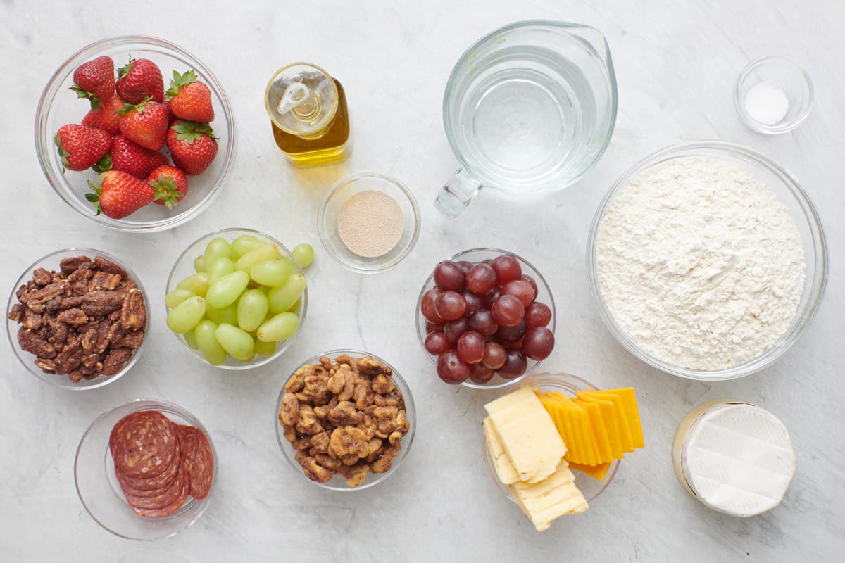 Ingredients for recipe: fresh strawberries, green and red grapes, candied pecans and walnuts, beef salami, sliced cheeses, brie wheel, oil, flour, salt, and yeast.