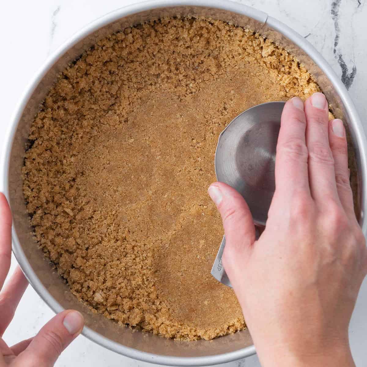 Pressing the crumbs into the pan with a metal measuring cup.