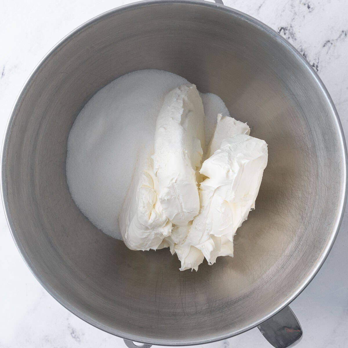 Cream cheese and sugar in the bowl of a stand mixer before mixing.