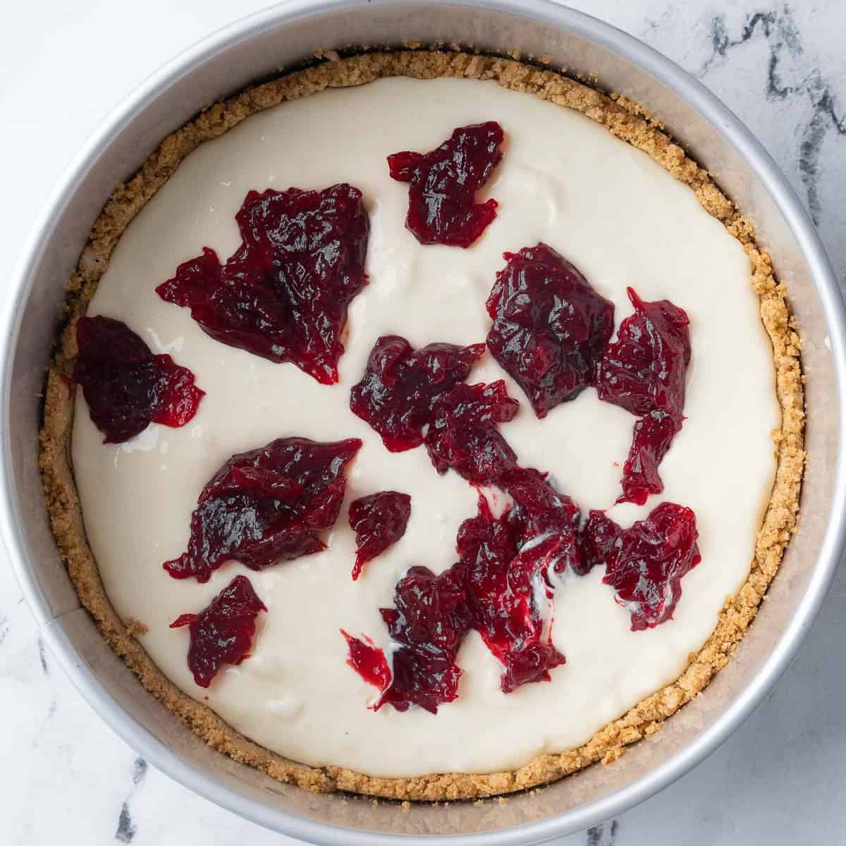 Half the cheesecake batter poured into the crust with spoonfuls of cranberry sauce added.