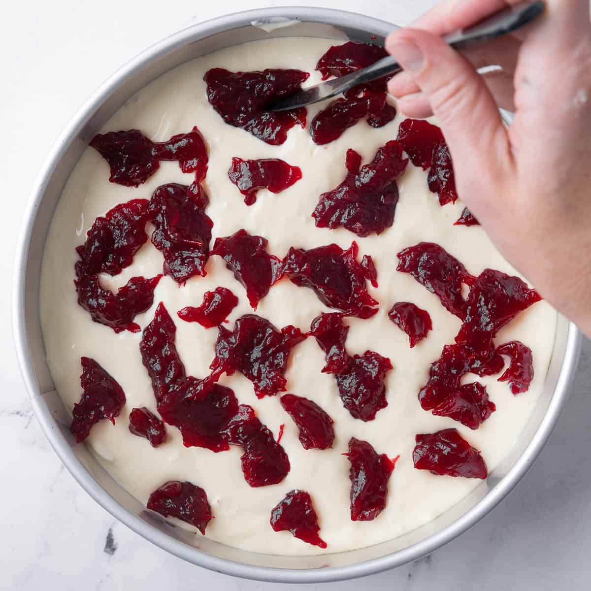 Remaining batter poured on top with cranberry sauce and a knife starting to swirl the sauce around.