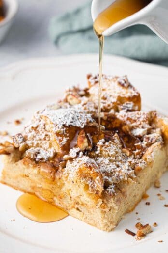 Slice of French toast casserole on a plate with syrup being poured over.