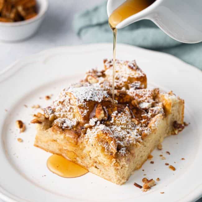 Slice of French toast casserole on a plate with syrup being poured over.
