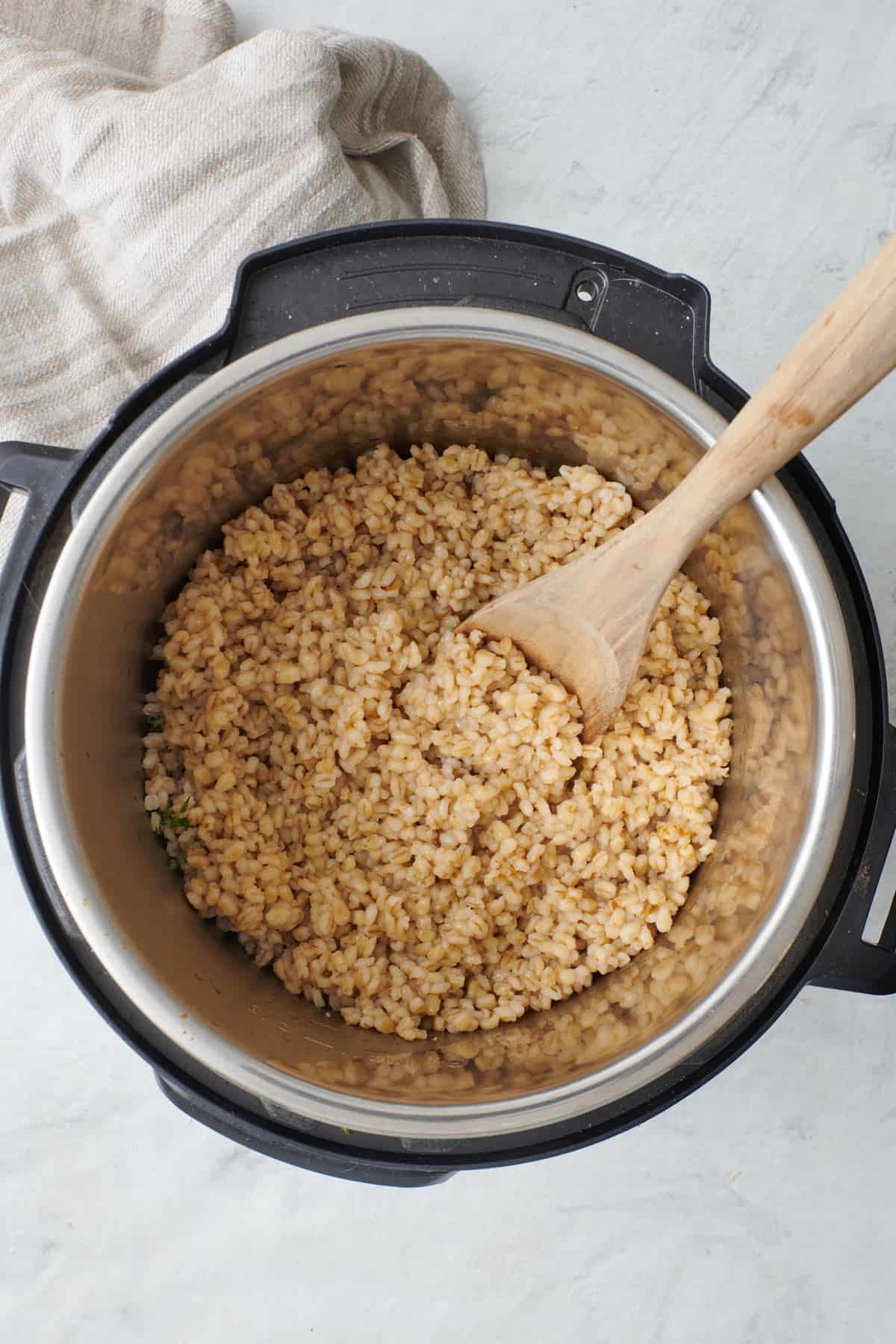 Barley in an instant pot after cooking with broth, wooden spoon dipped inside.