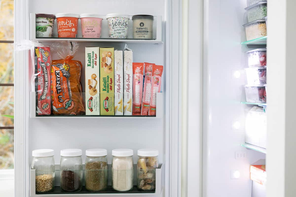 Freezer door organized with ice cream, breads, snacks, and jars of spices and other foods.