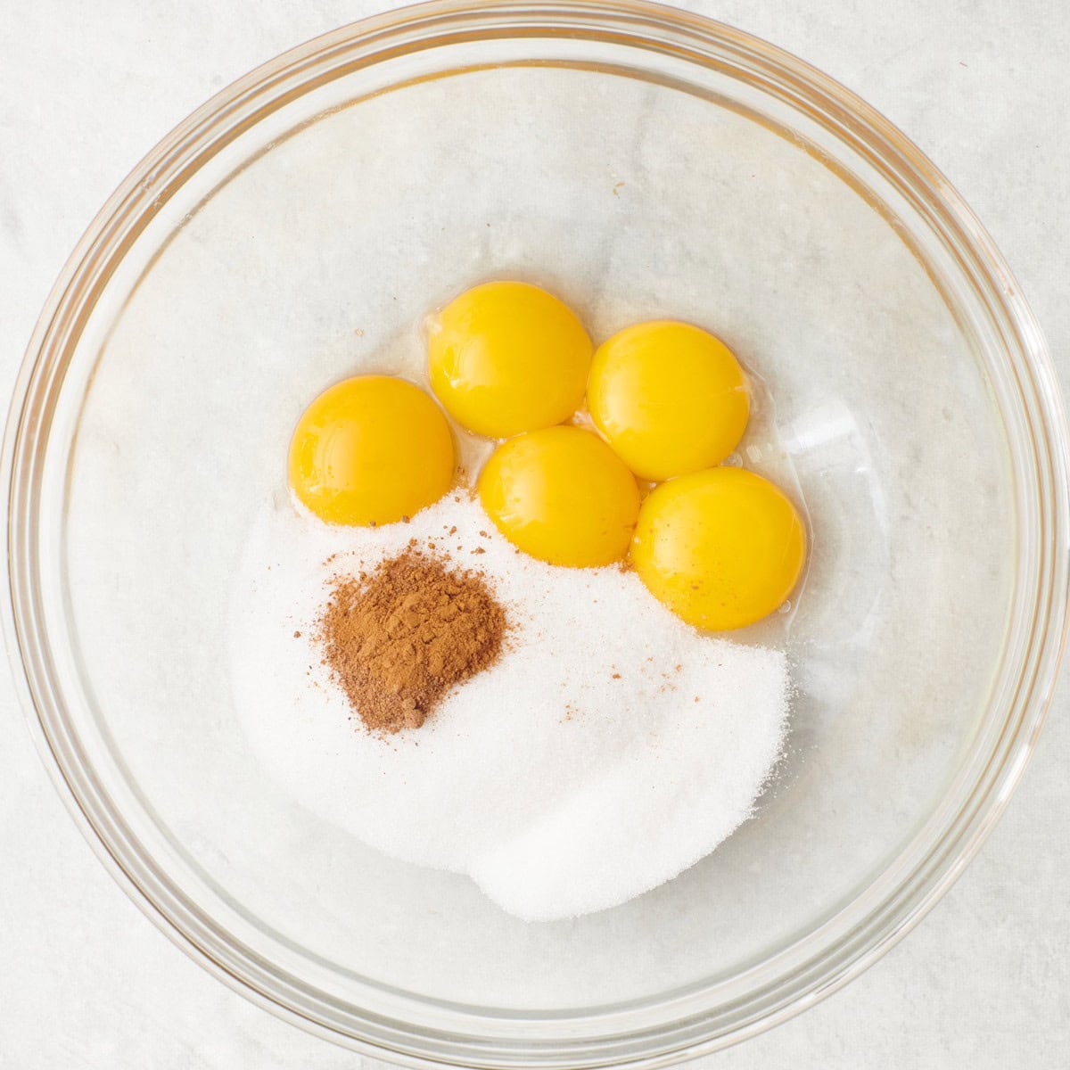 Egg yolks, sugar, nutmeg, and cinnamon in a bowl before whisking.