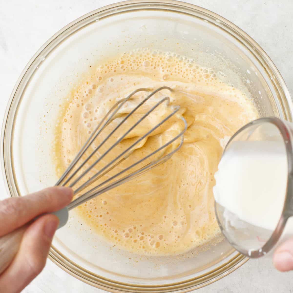 Pouring in some milk to the egg mixture bowl while whisking to temper.