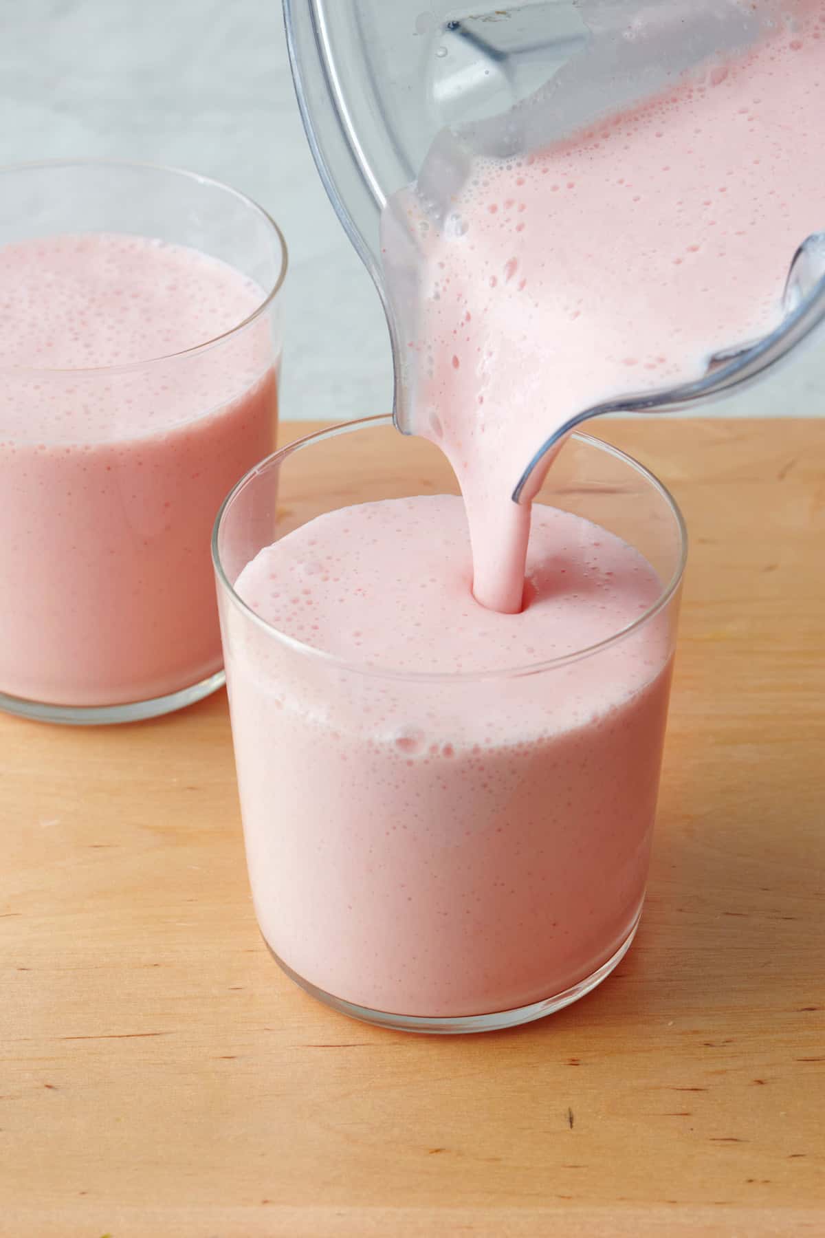 Pouring strawberry yogurt smoothie into a small glass.