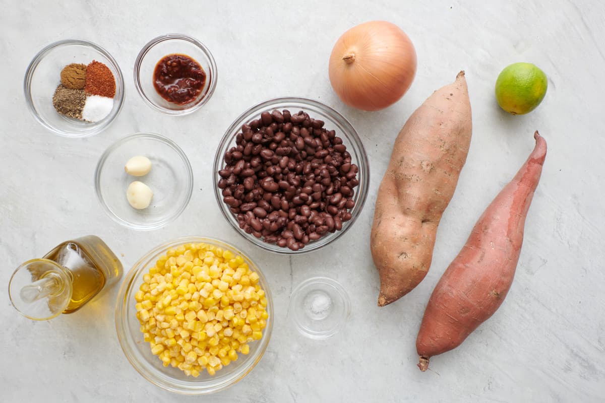 Ingredients for recipe before prepping: spices, chopped chipotle peppers, garlic, oil, corn, black beans, onion, salt, sweet potatoes, and lime.