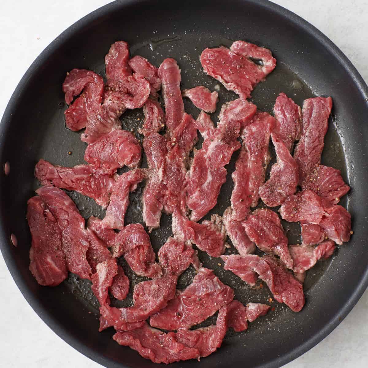 Beef spread in an even layer in an oiled skillet before cooking.