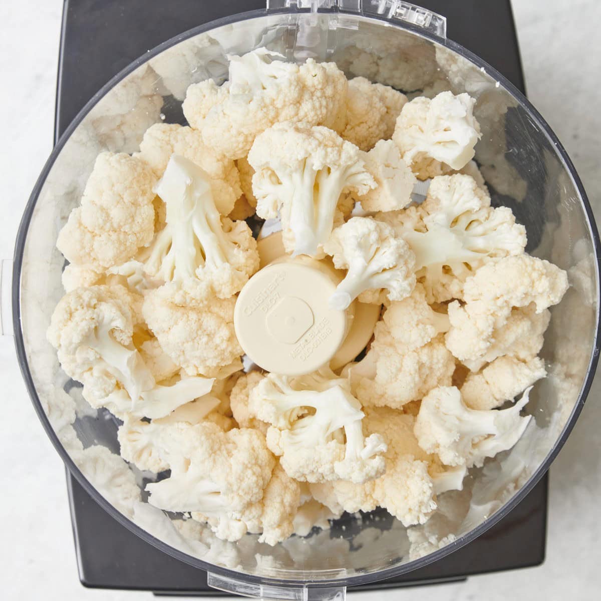Cauliflower florets in the bowl of a food processor before pulsing,
