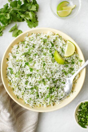 Cilantro lime rice in a bowl with a few lemon wedges and a spoon dipped in.