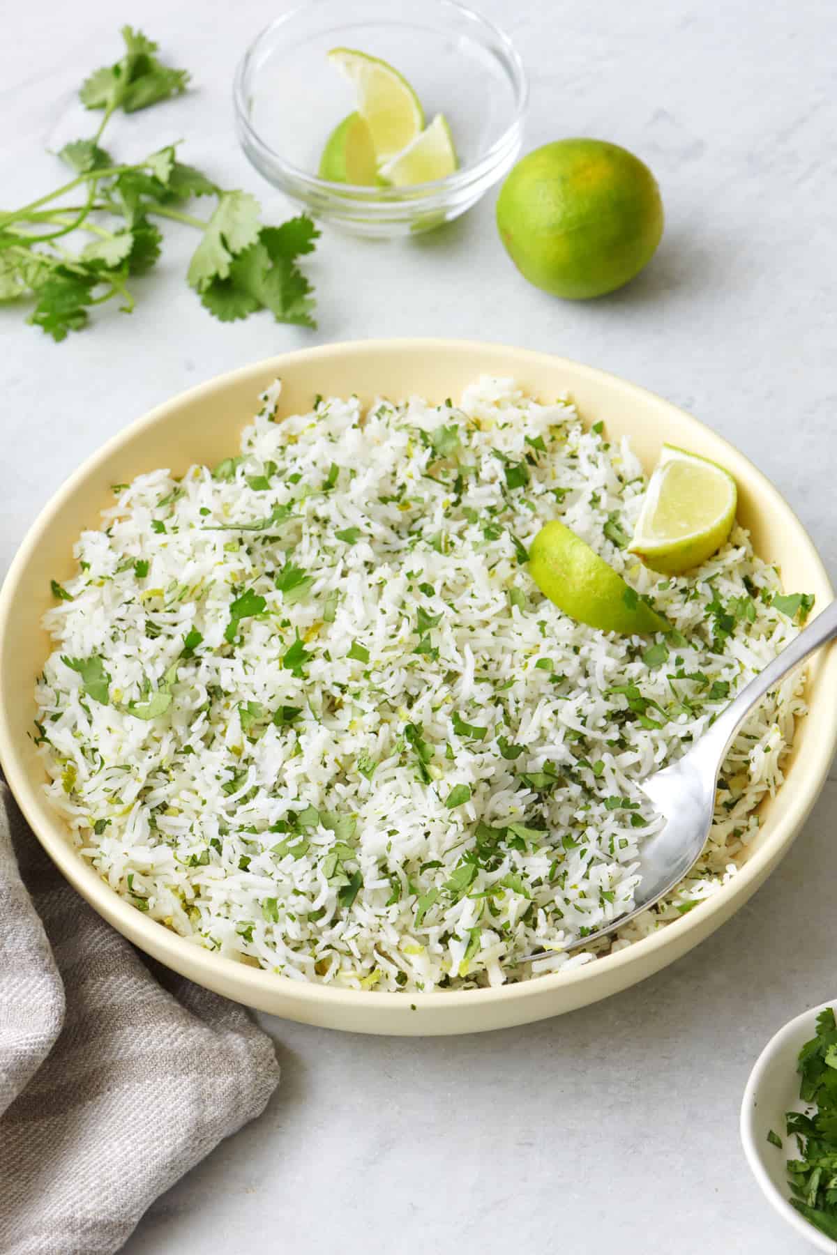 Cilantro lime rice in a bowl with a few lemon wedges, a spoon dipped in, and a small dish of more lime wedges and a whole lime nearby.