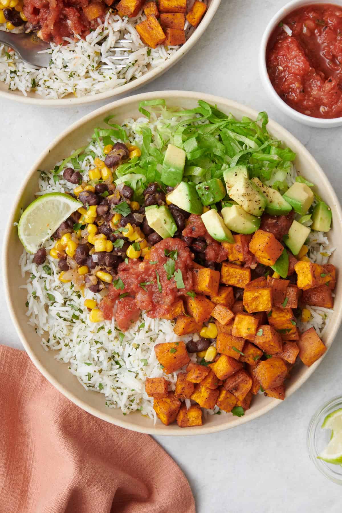 A bowl of cilantro lime rice topped with a black bean salsa, salsa, sweet potatoes, avocado, and lettuce.