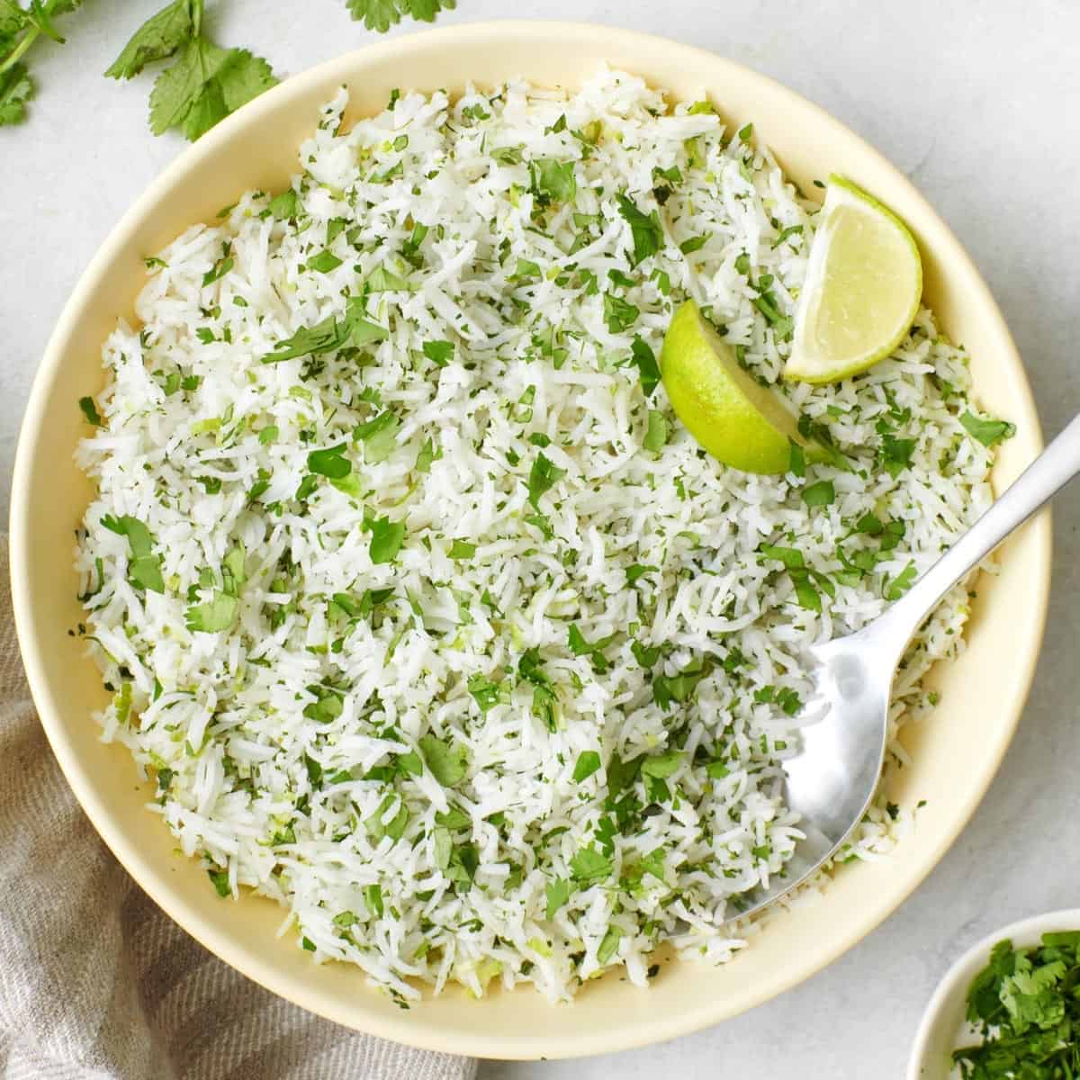 Cilantro lime rice in a bowl with a few lemon wedges and a spoon dipped in.